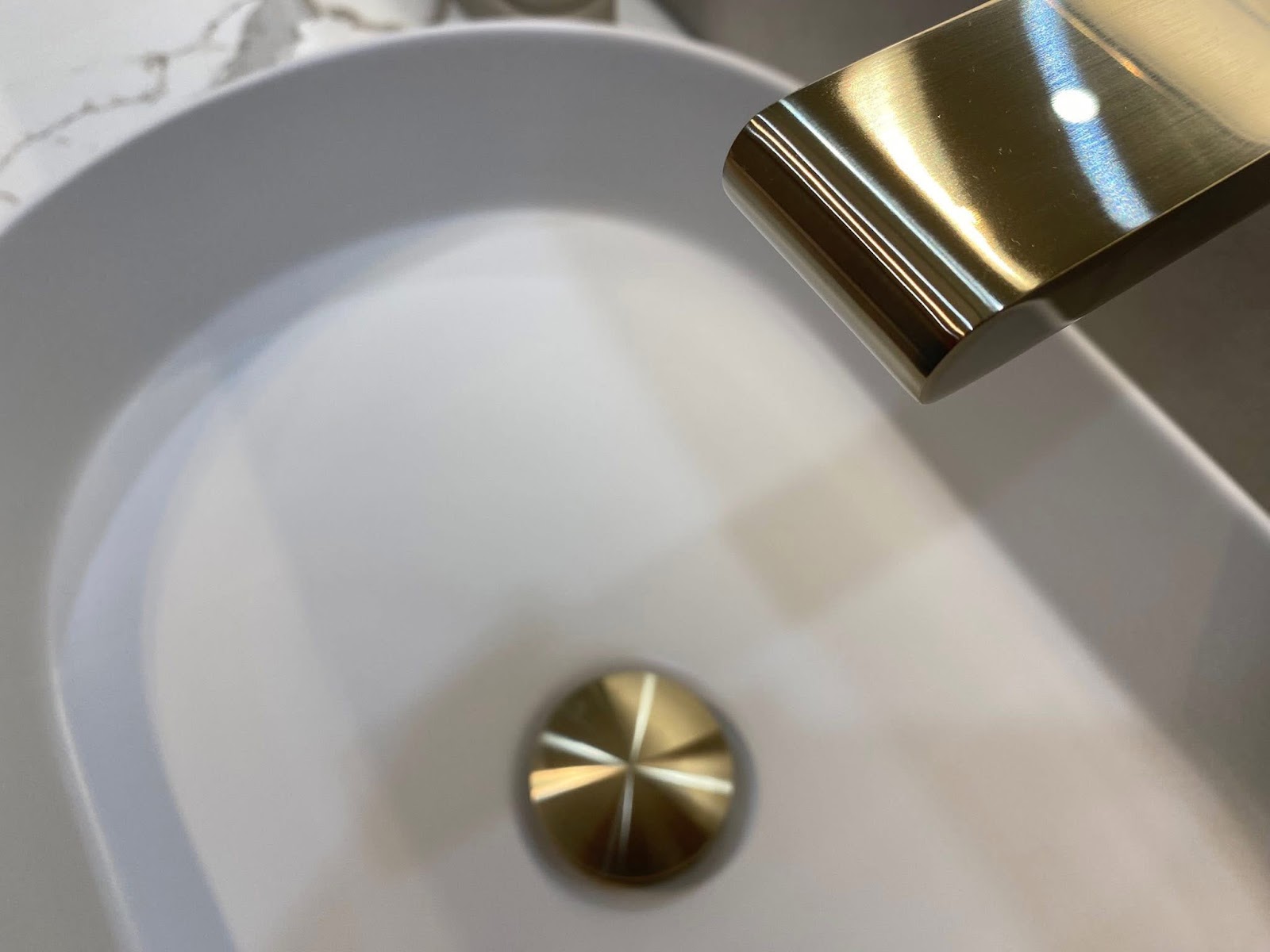 Close up of a white basin and brushed brass tap, polished